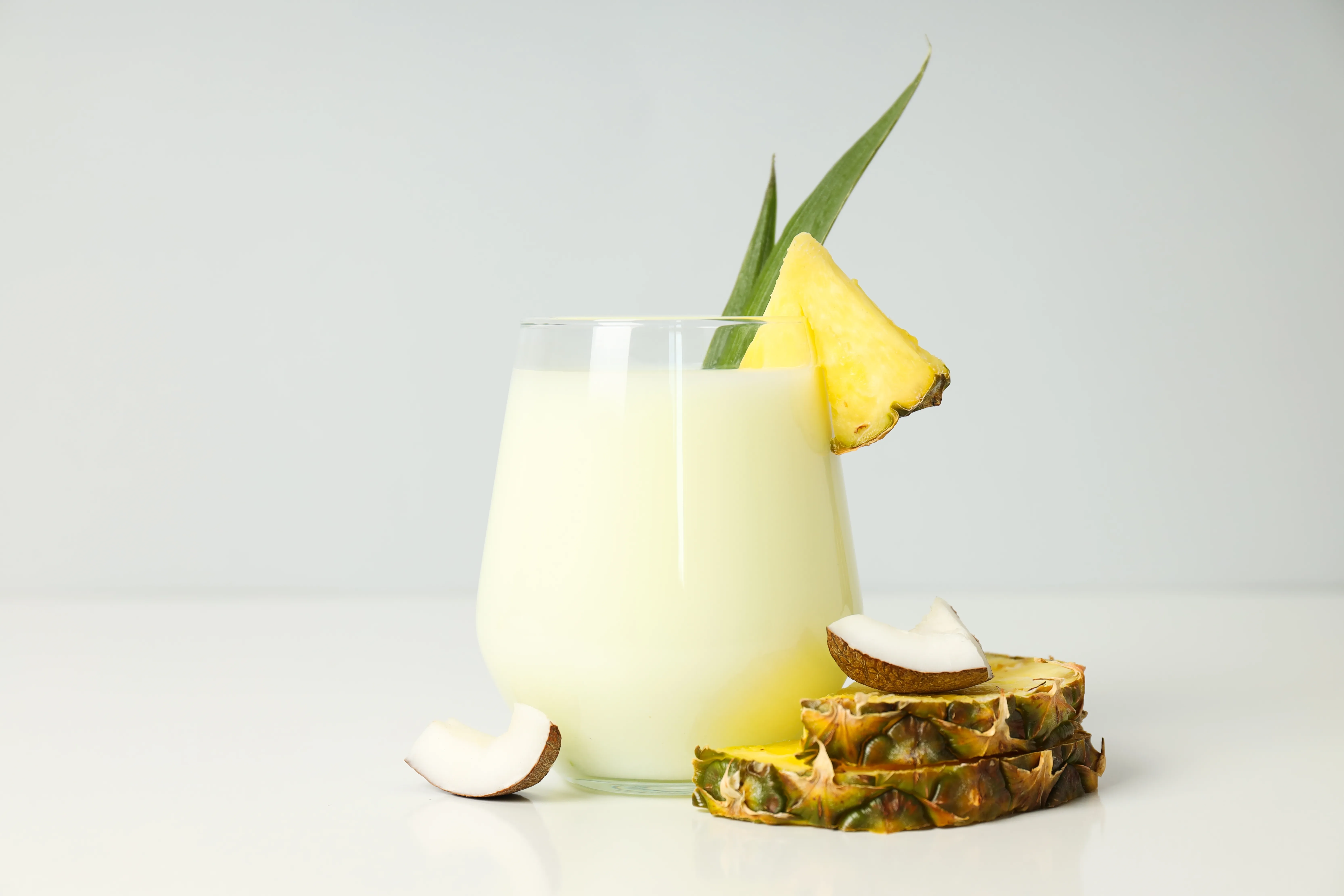 A glass of creamy coconut and pineapple mocktail, garnished with a pineapple wedge and fresh coconut pieces.