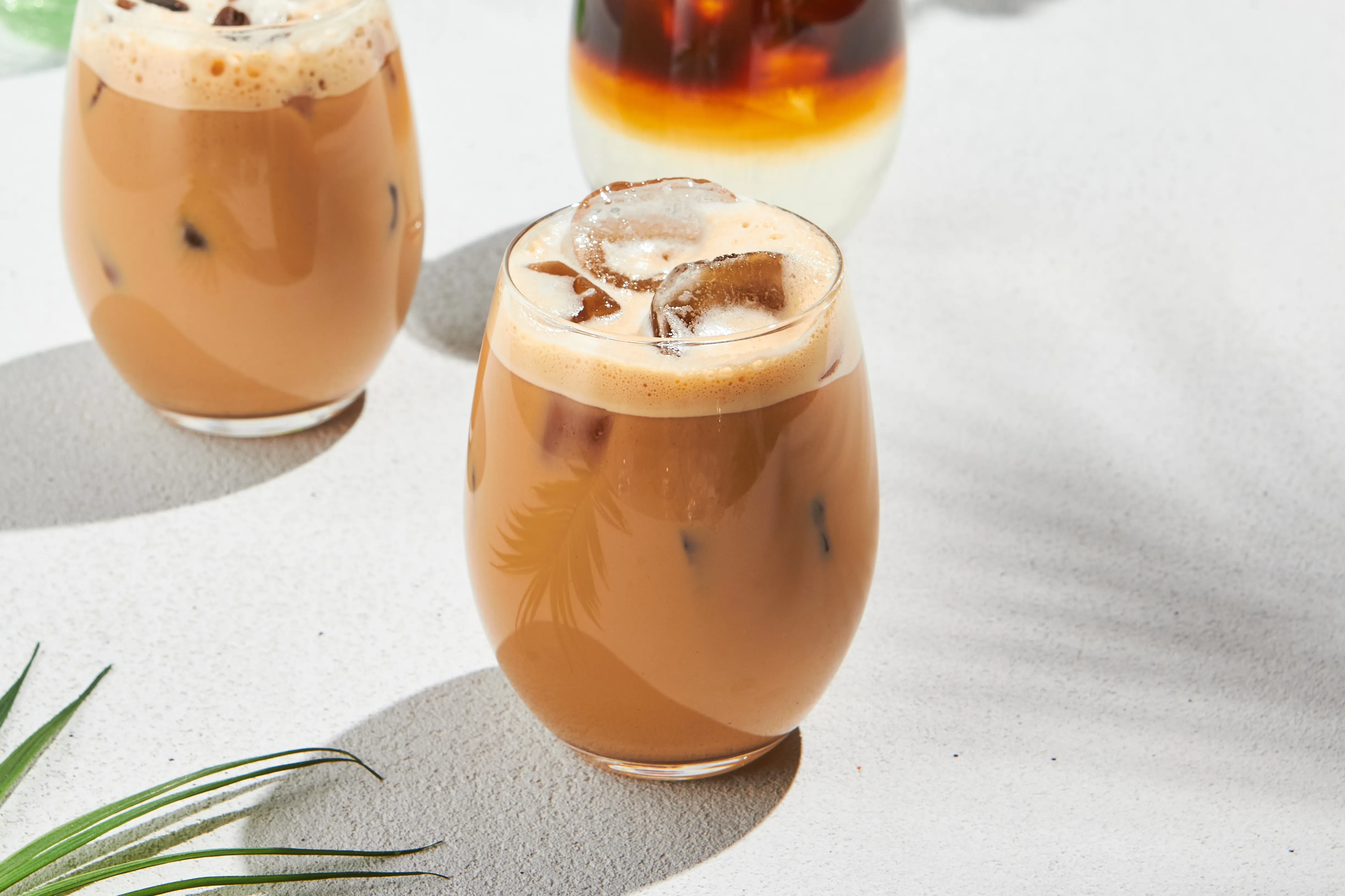 A glass of iced coffee or latte macchiato with ice cubes and a frothy top layer, highlighted by sunlight.