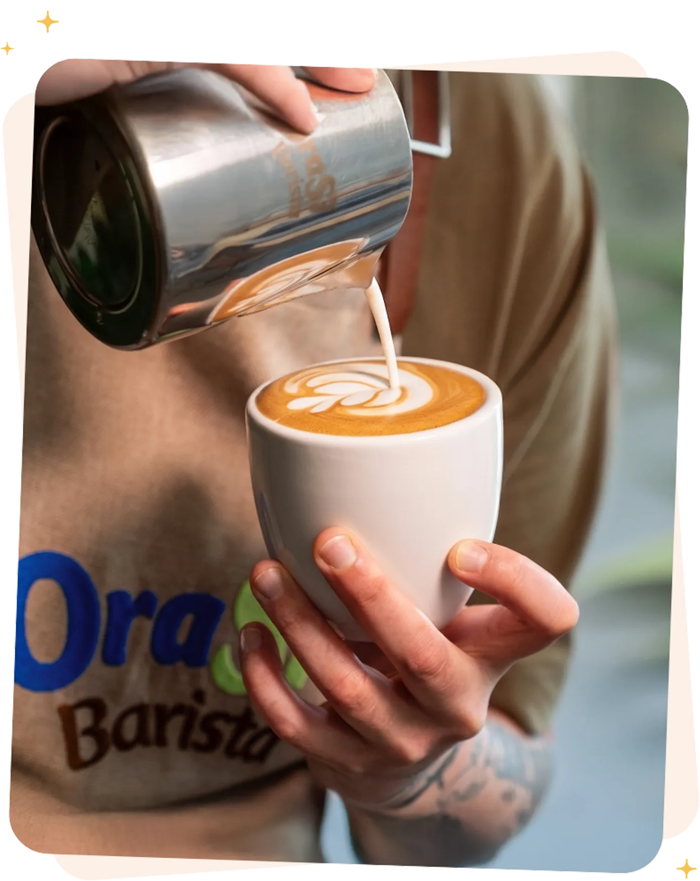 Ragazzo con la maglia di OraSì che sta versando del cappuccino dentro ad una tazza bianca